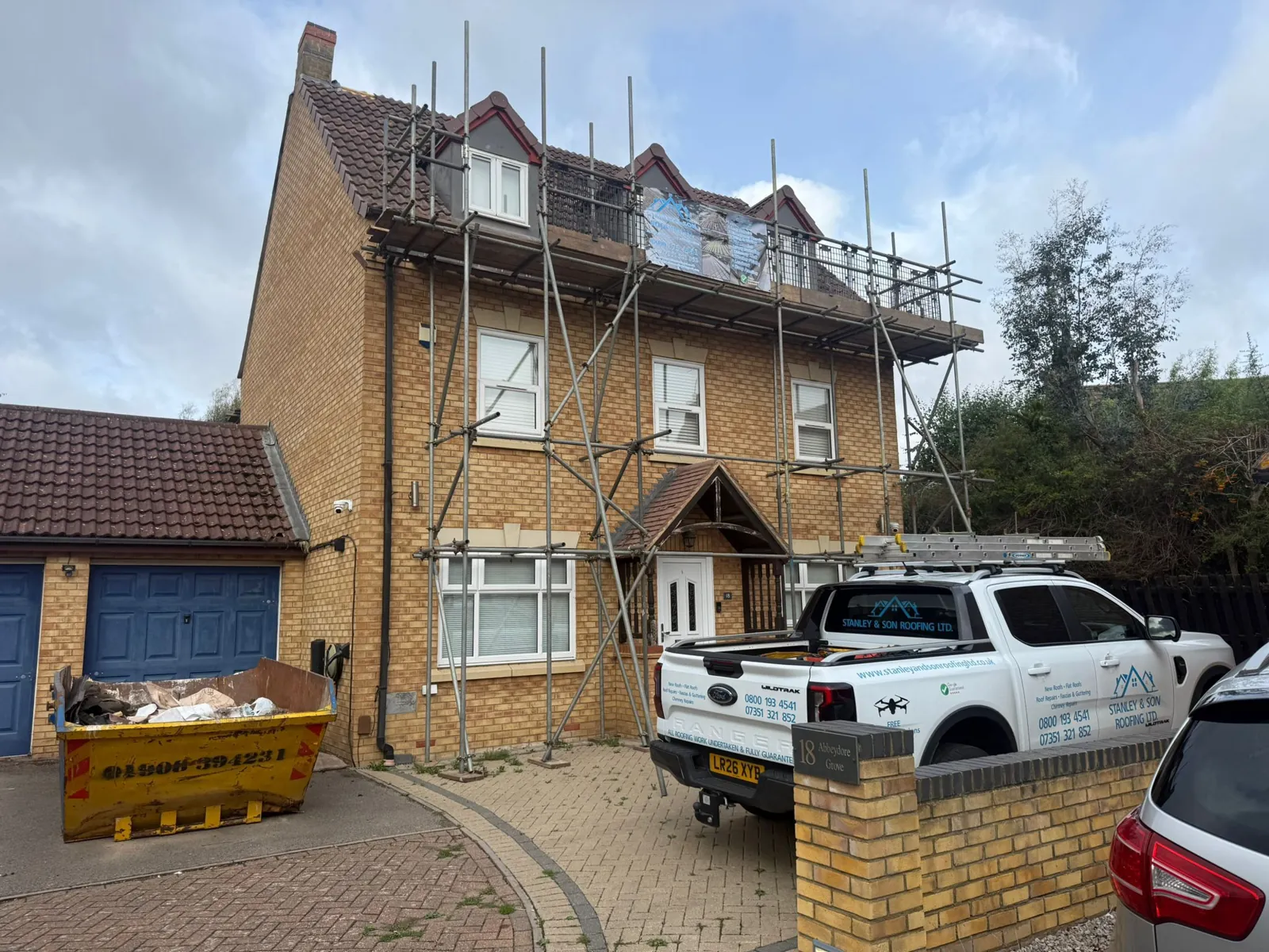 Three-storey detached house in Milton Keynes fully scaffolded for a re-roof, with the Stanley & Son Roofing pick-up on the drive
